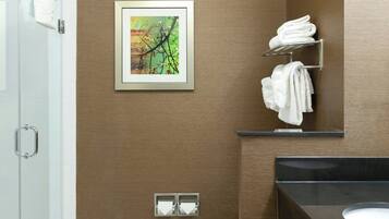 Et moderne badeværelse med glasvæg omkring bruseren, toilet og et underskab med vask.
