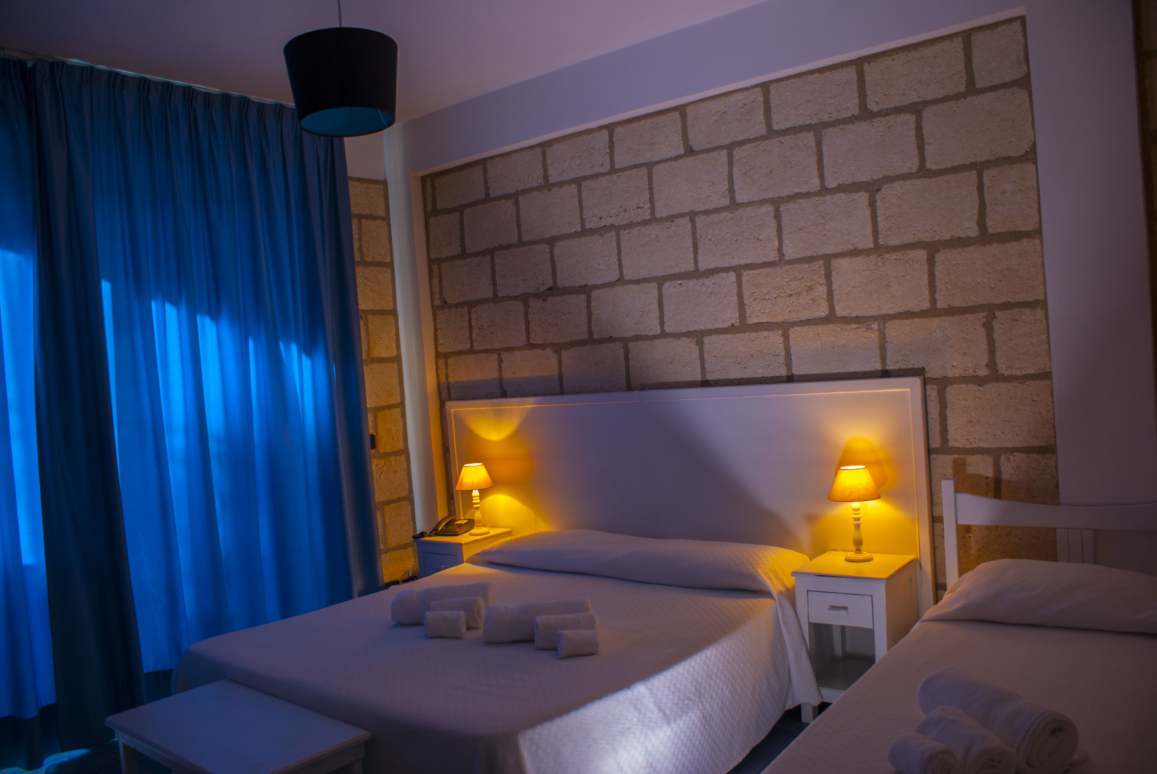 Une chambre d’hôtel avec un lit double, deux tables de chevet avec des lampes, une petite table et un rideau bleu.
