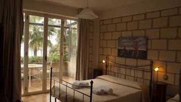 A bedroom with a bed, a nightstand, a lamp, a painting, and a sliding glass door leading to a patio with a table and chairs.