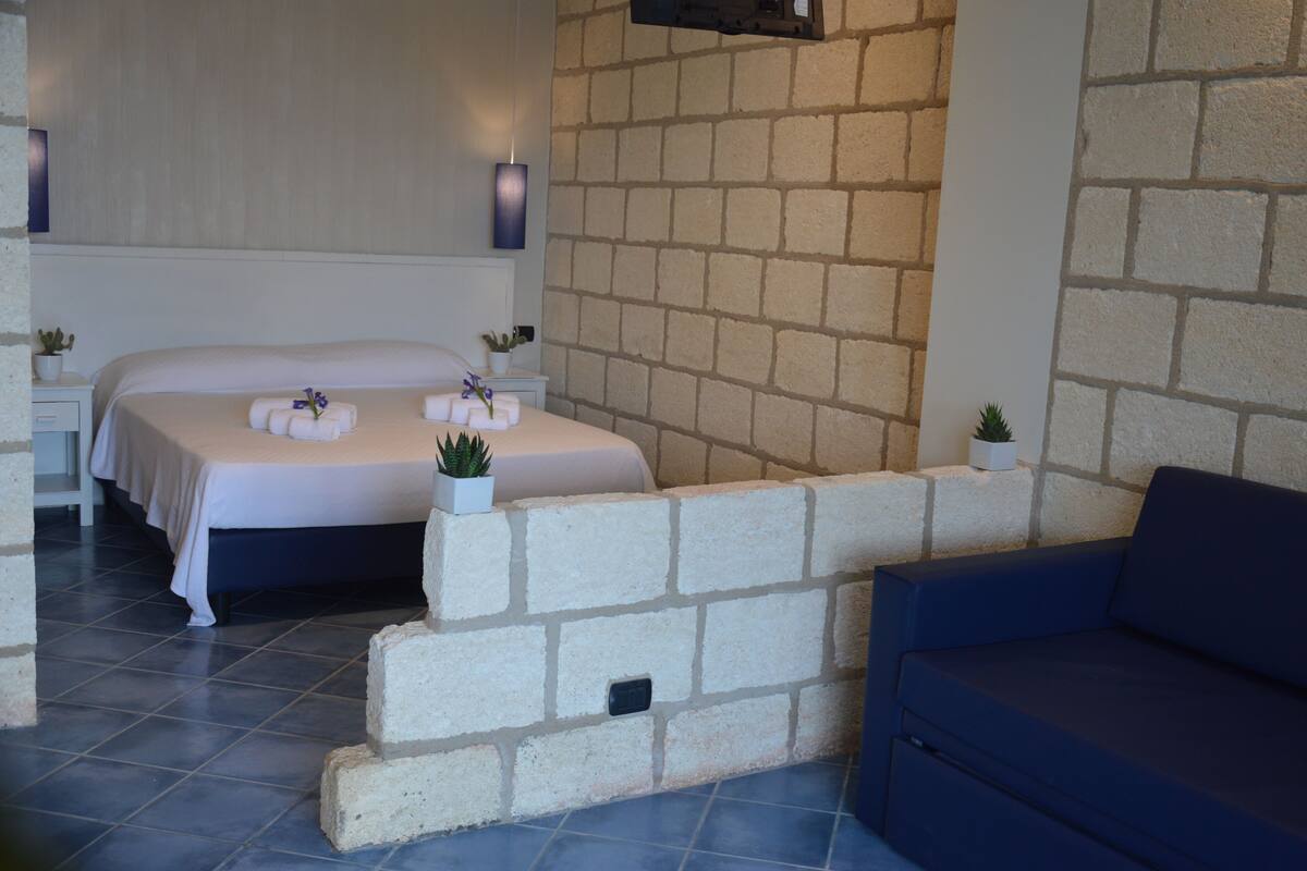 A bedroom with a bed, a blue sofa, and a brick wall.