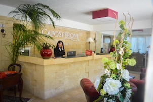 Un mostrador de recepción con un letrero que dice "CAPOSPERONE", una computadora portátil, un florero rojo y una planta en maceta.