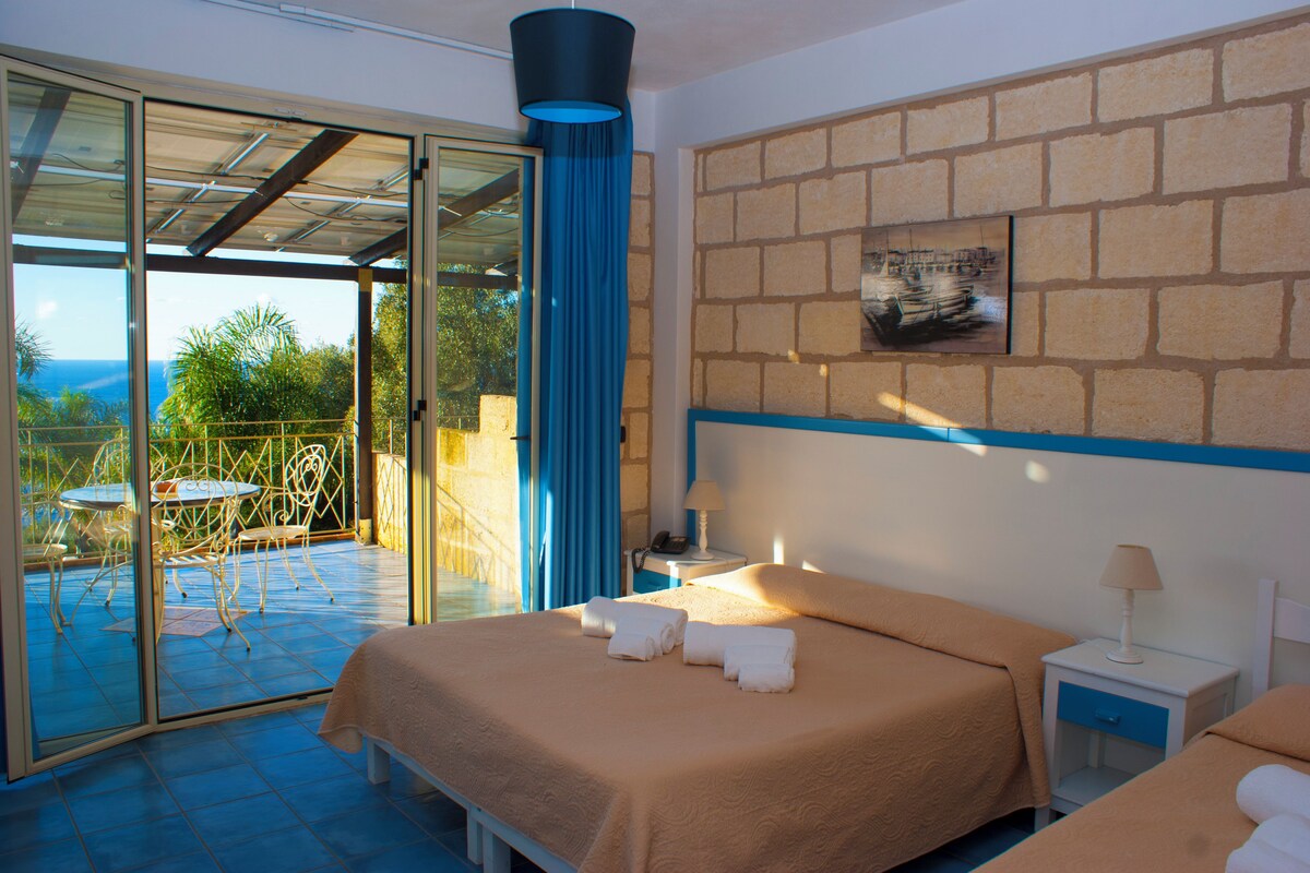 A hotel room with a bed, a nightstand, a chair, and a table with a view of the outdoors.