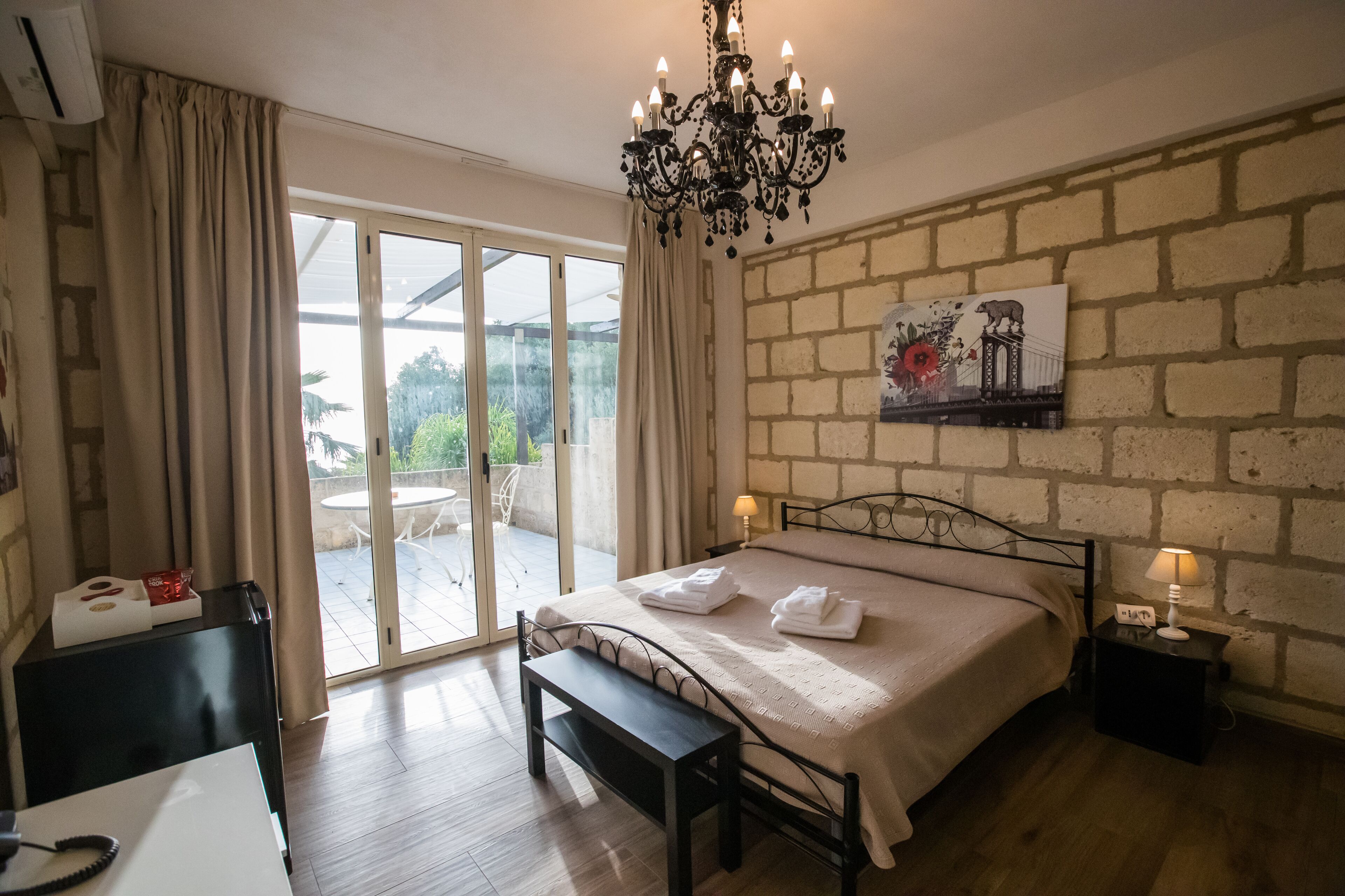 Une chambre à coucher comprenant un lit, un banc, une table de chevet avec une lampe, un tableau accroché au mur et une porte-fenêtre coulissante donnant sur un espace extérieur.