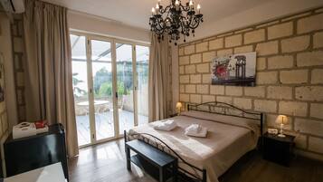 Une chambre à coucher comprenant un lit, un banc, une table de chevet avec une lampe, un tableau accroché au mur et une porte-fenêtre coulissante donnant sur un espace extérieur.