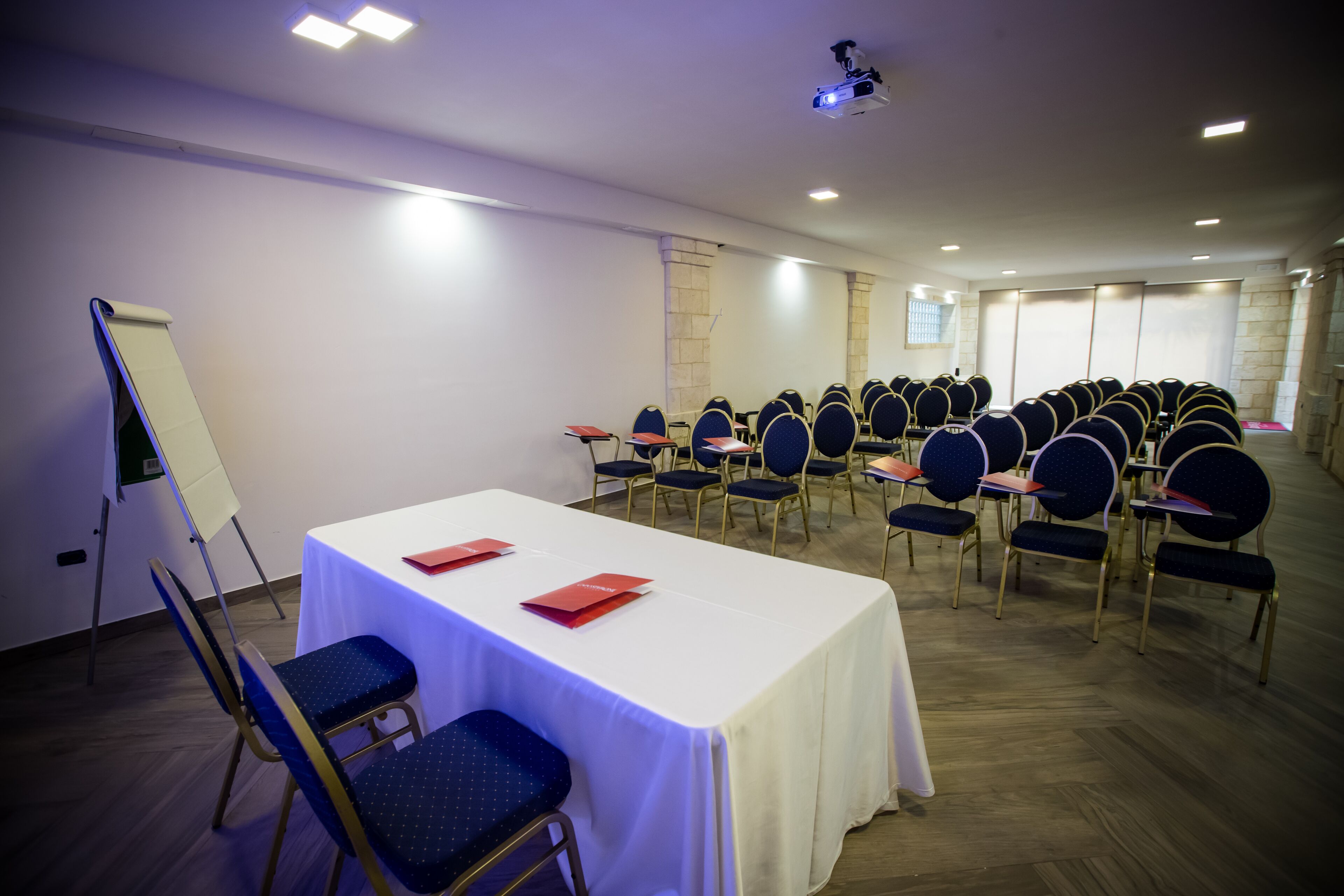 Una sala conferenze con un lungo tavolo, file di sedie, una lavagna e un proiettore.