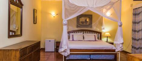 A bedroom with a four-poster bed, a wooden dresser, a ceiling fan, and a nightstand with a lamp.