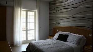 Un dormitorio con cama, mesita de noche, ventana con cortinas y pared con diseño ondulado.