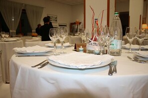 A dining table set with white tablecloths, plates, cutlery, and wine glasses.