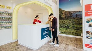 A reception desk with a sign that reads "Tickets & Tours" and a backdrop with a scenic landscape. - Kinlay Hostel Galway (Galway)