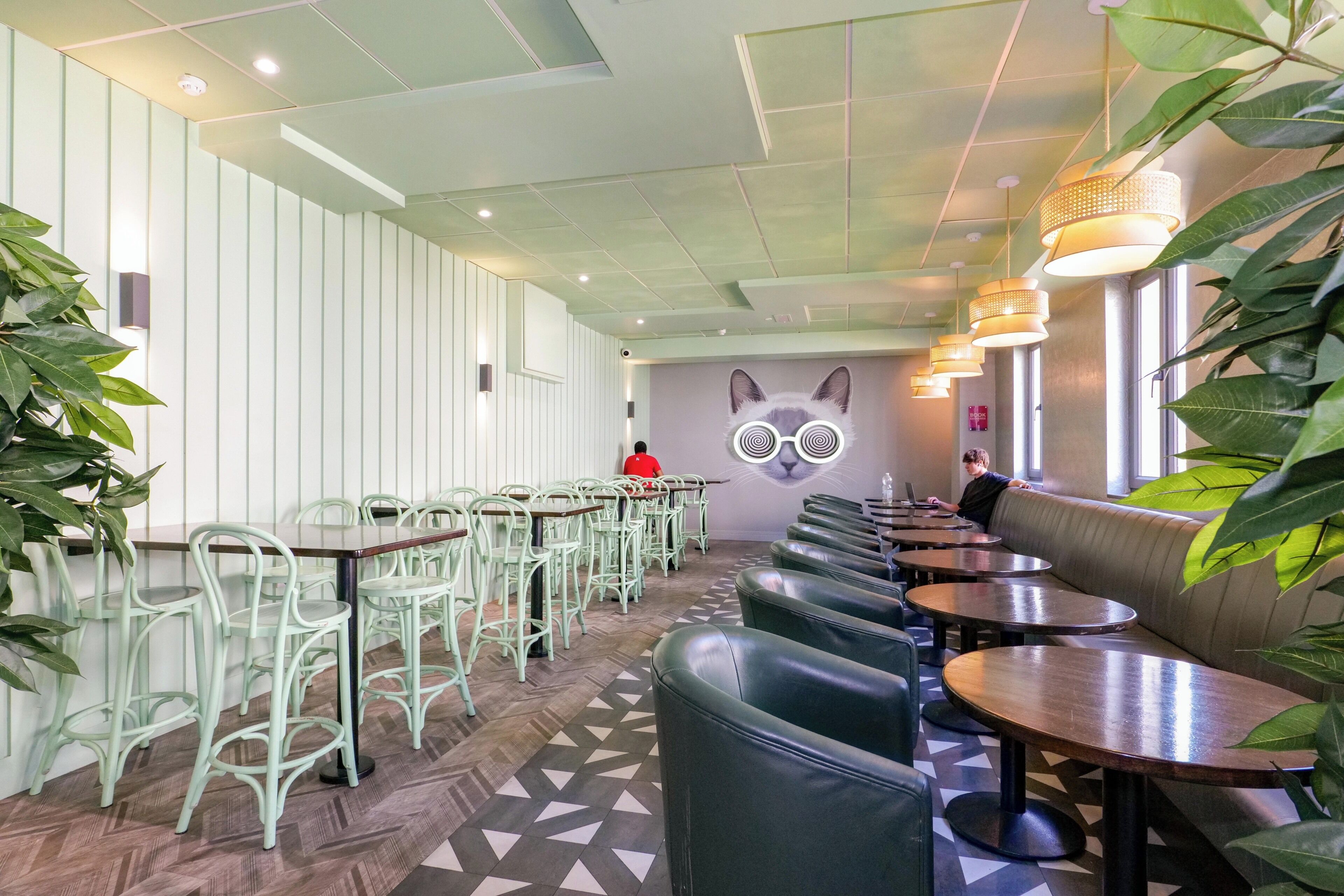 A restaurant with green chairs, round tables, and a wall mural.
