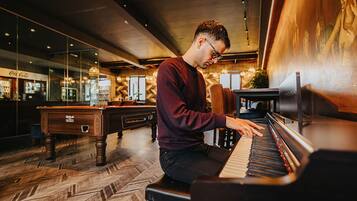 A man playing a piano in a room with a billiards table and a wall with a mural.