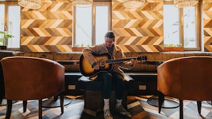 A person playing an acoustic guitar in a room with a chevron-patterned wall and a herringbone floor. - Kinlay Hostel Galway (Galway)