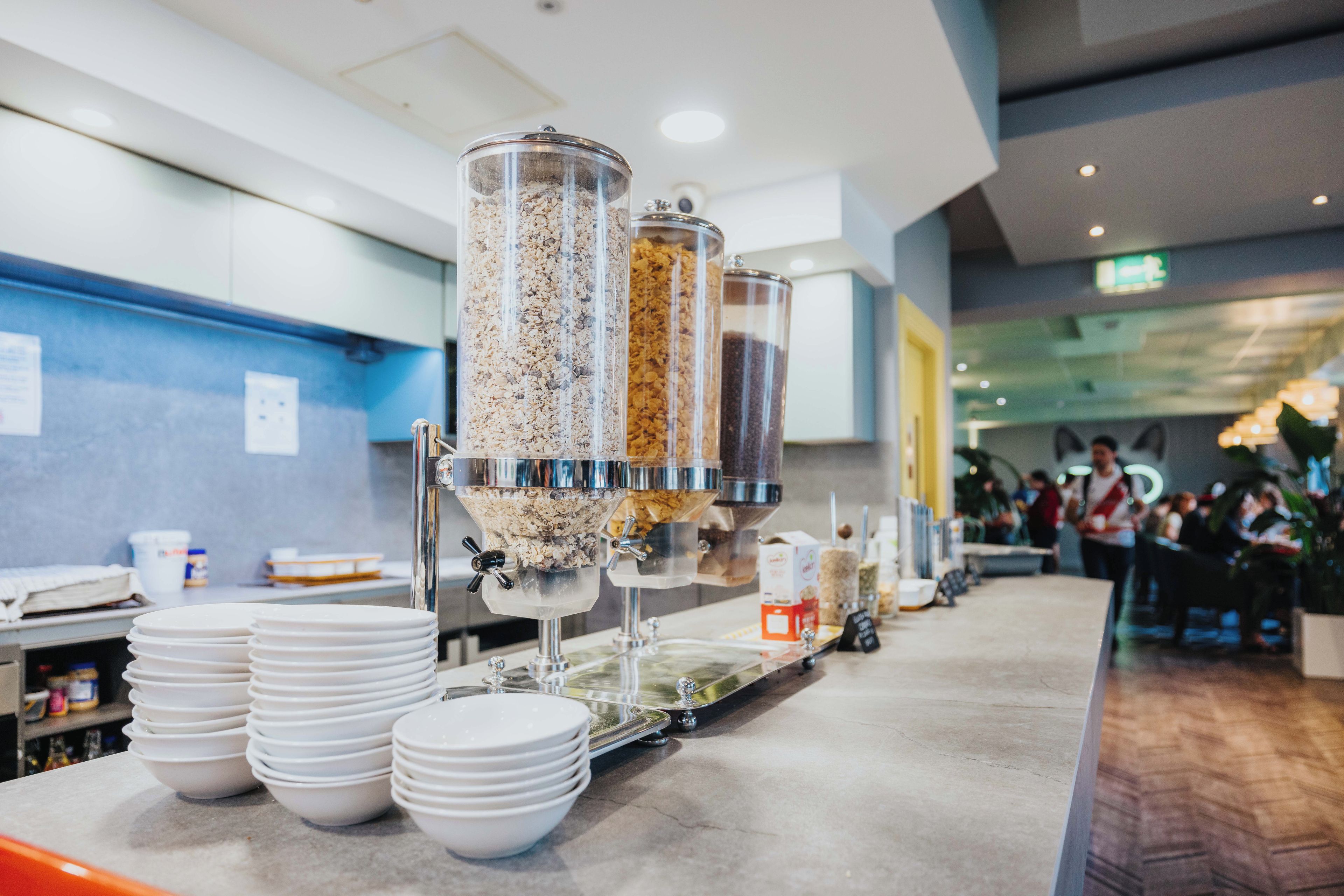 Zona de buffet amb diversos distribuïdors d'aliments i plates blancs apilades.