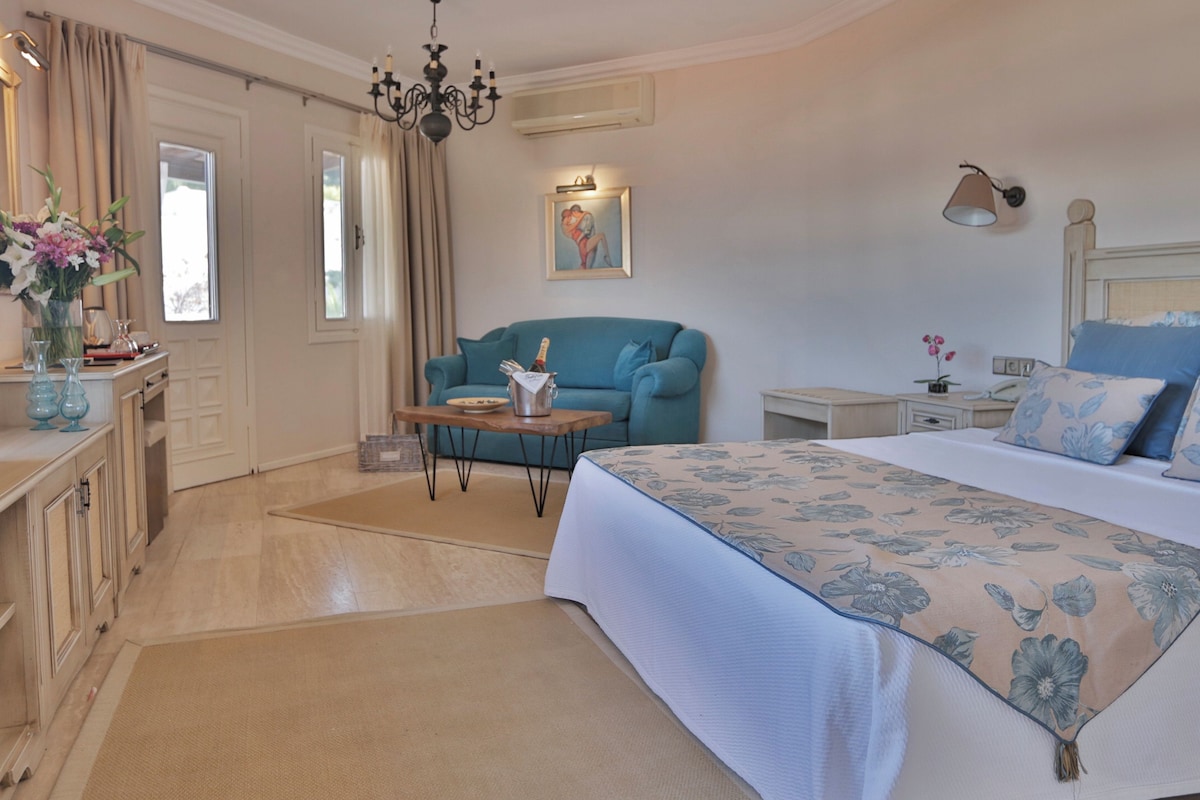 Ein Schlafzimmer mit einem Bett, einem blauen Sofa, einem kleinen Tisch mit einer Flasche, einem Bild an der Wand und einer Chandelieber.