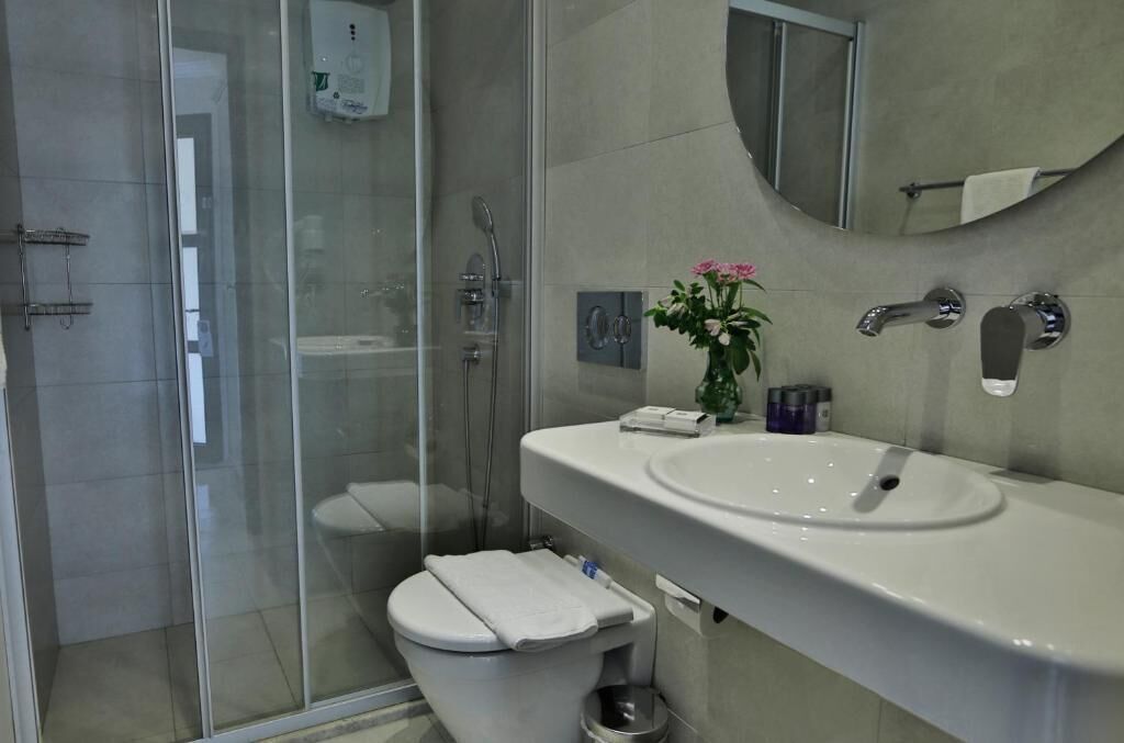 Un bany modern amb una dutxa de vidre, un vàter blanc, un lavabo amb mirall i un ram de flors.