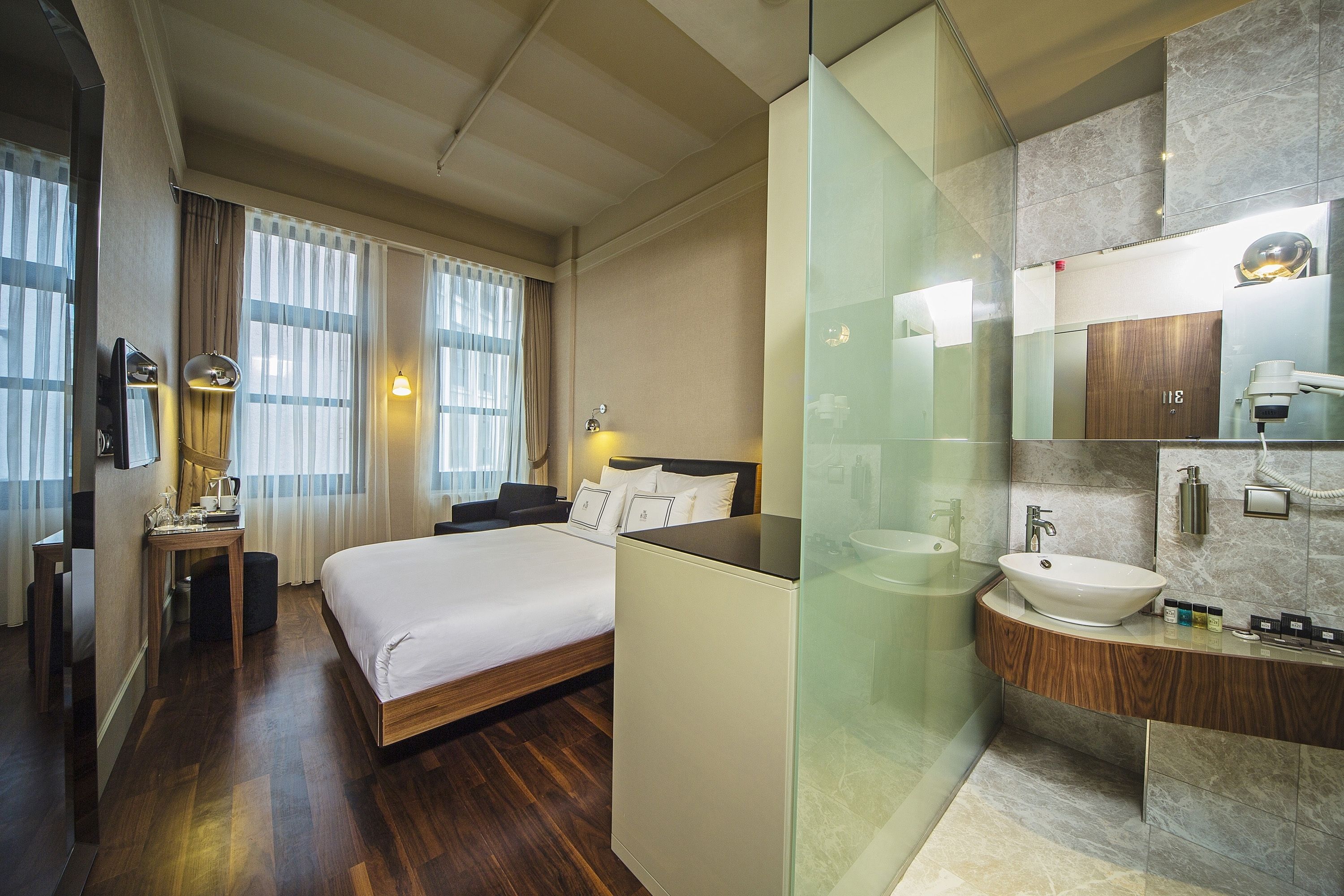 Quarto de hotel com cama, mesa de cabeceira, luminária e banheiro com pia, espelho e amenities.