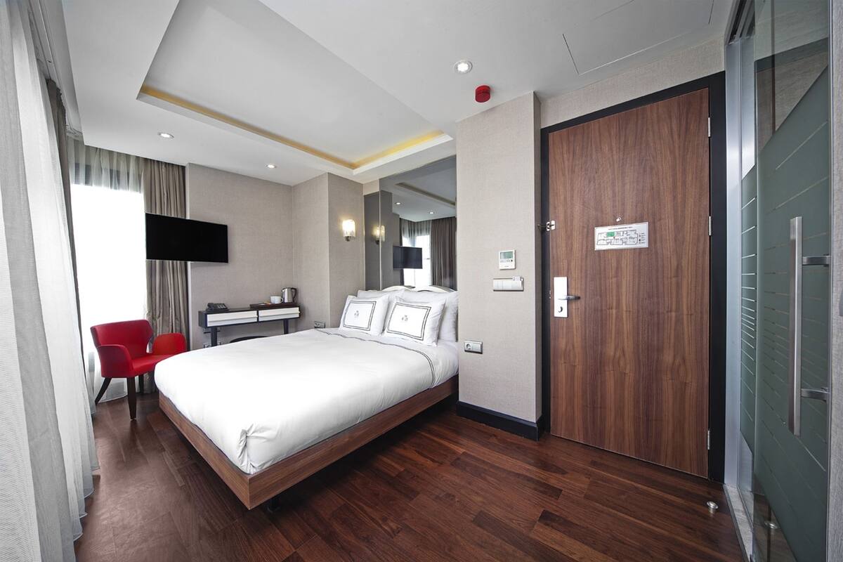 A hotel room with a bed, a desk, a chair, a TV, and a wooden door.