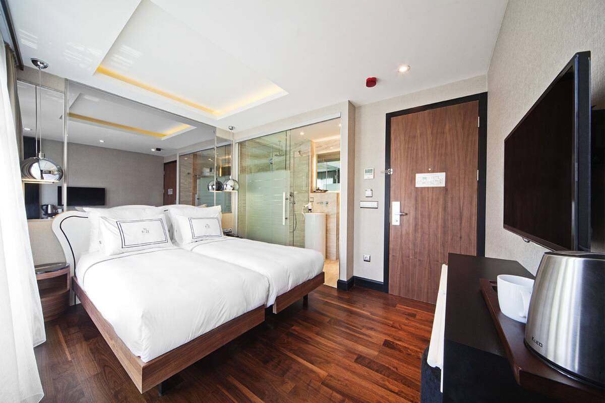 A modern hotel room with a large bed, a desk with a kettle, and a television.