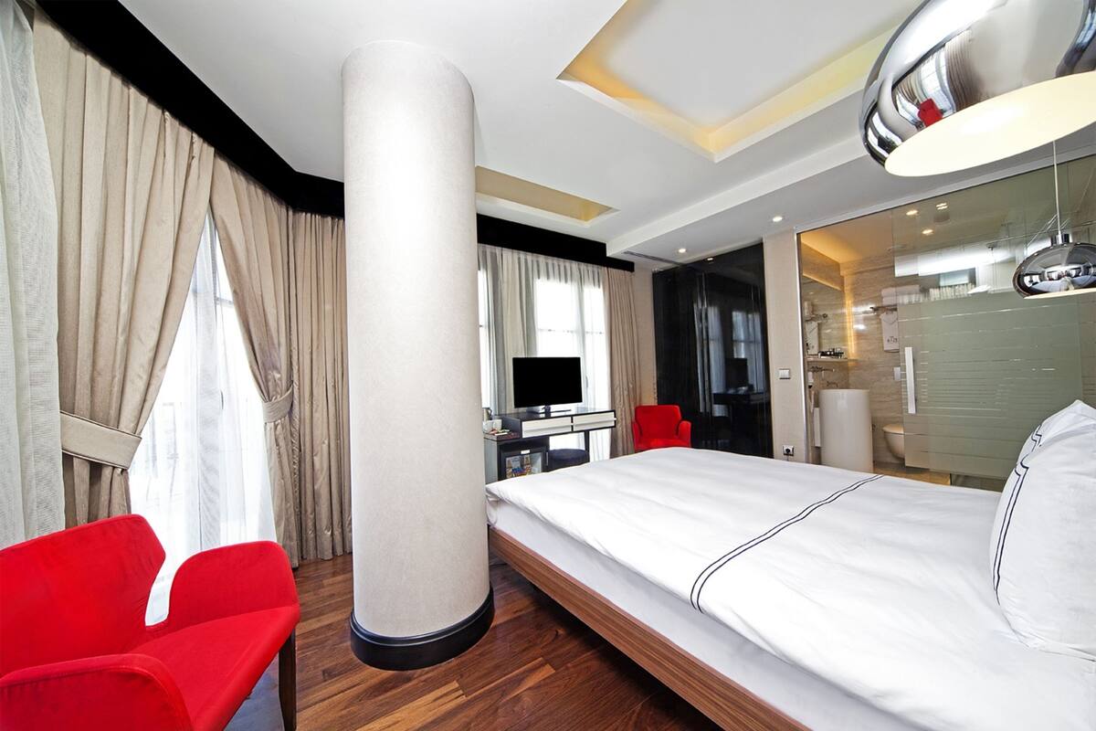 A hotel room with a bed, a desk, a chair, a large pillar, and a bathroom visible through an open door.