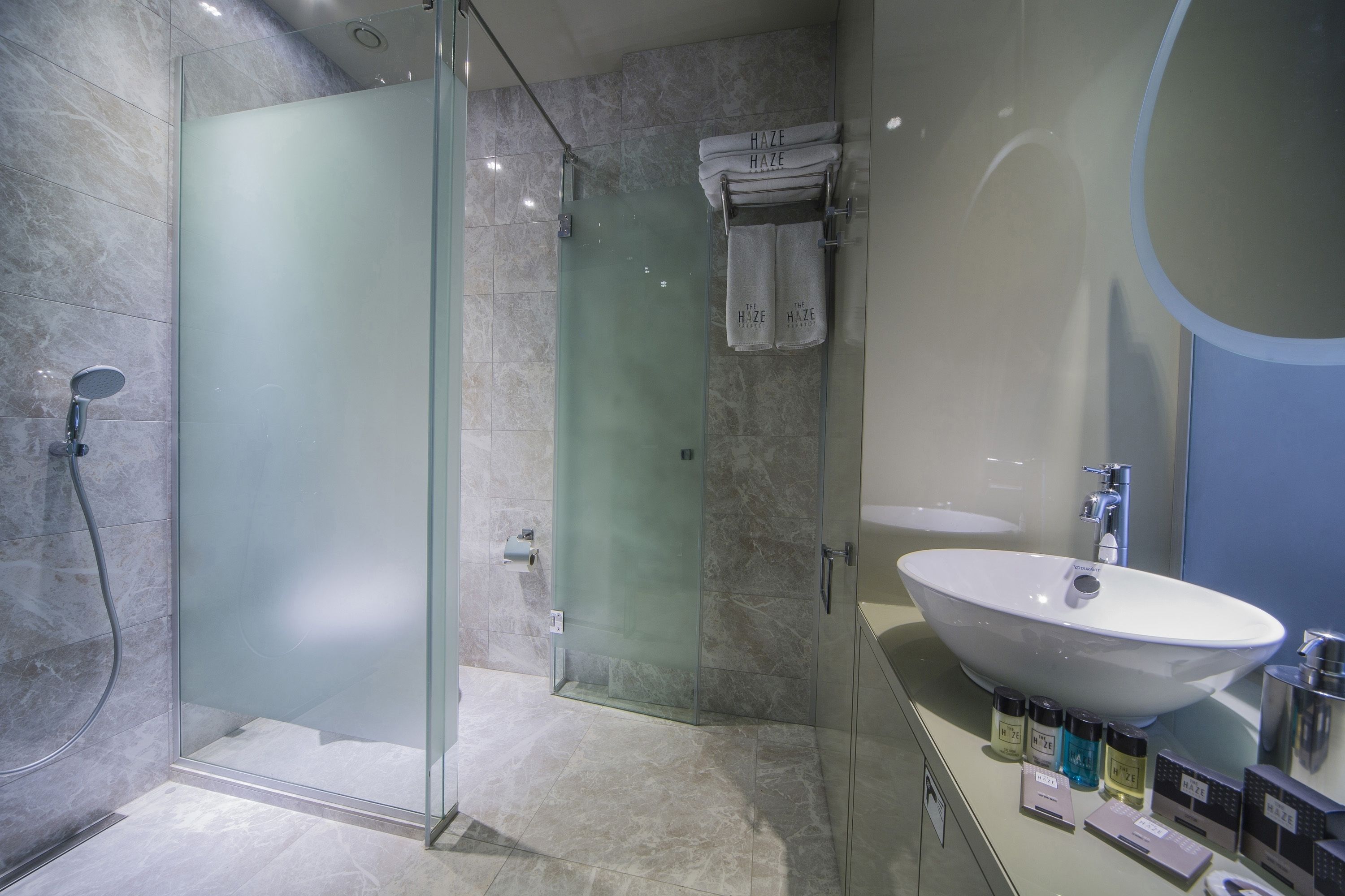 A modern bathroom with a glass-enclosed shower, a large white sink, and a mirror with a circular design.