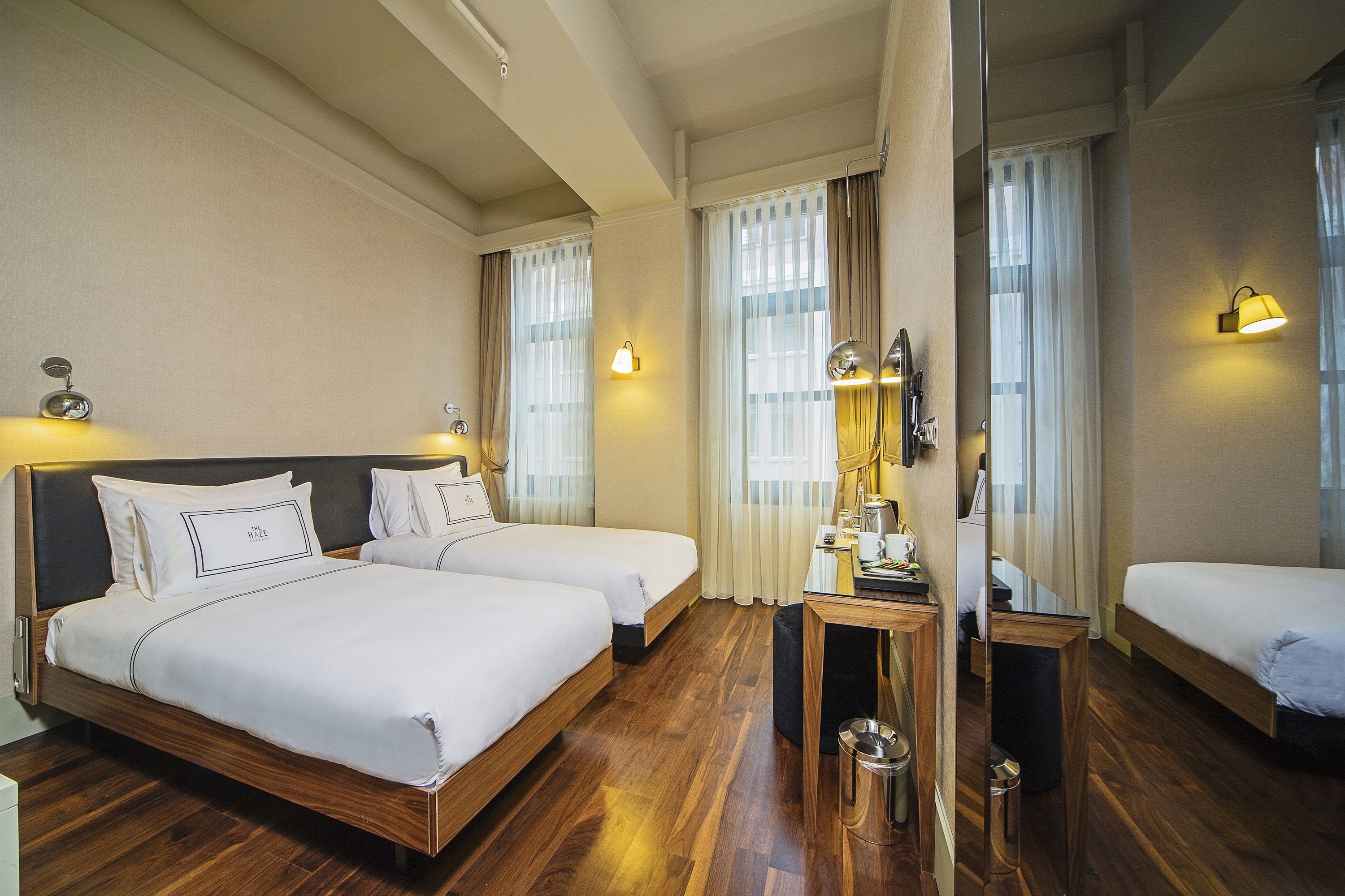 Habitación de hotel con dos camas, piso de madera y un espejo que refleja el ambiente.