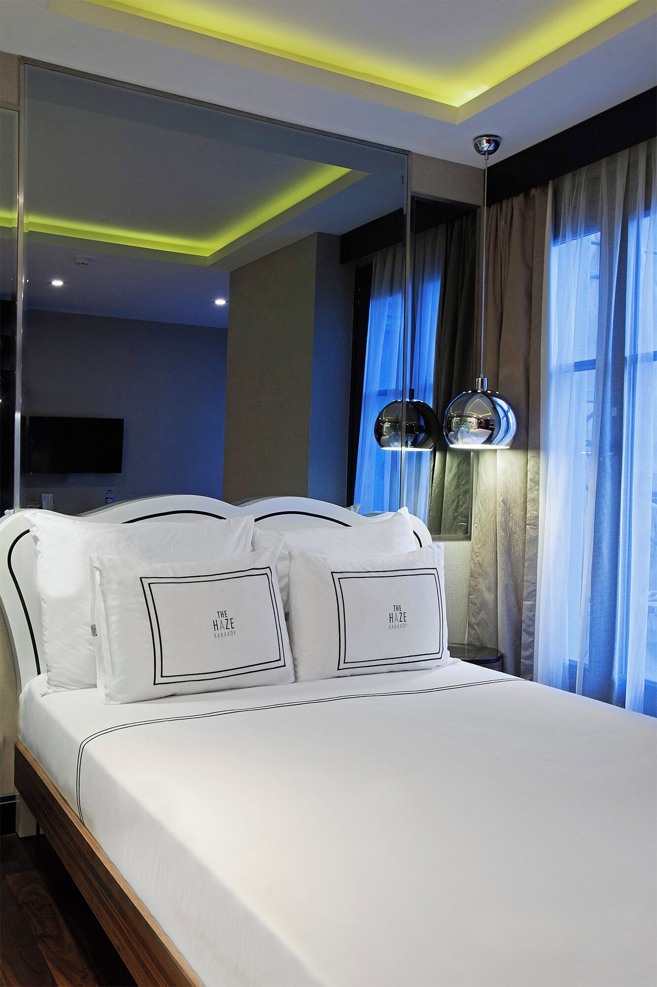 A modern hotel room with a large bed, a mirror, and a ceiling light fixture.