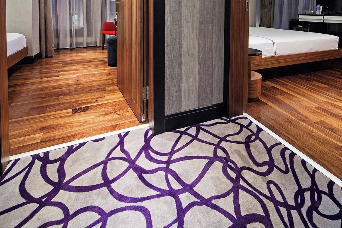 A hotel room with a wooden floor, a bed, a desk, a chair, and a large mirror.