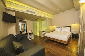 Habitación de hotel con una cama grande, un sofá, un televisor, un espejo y una pequeña kitchenette.