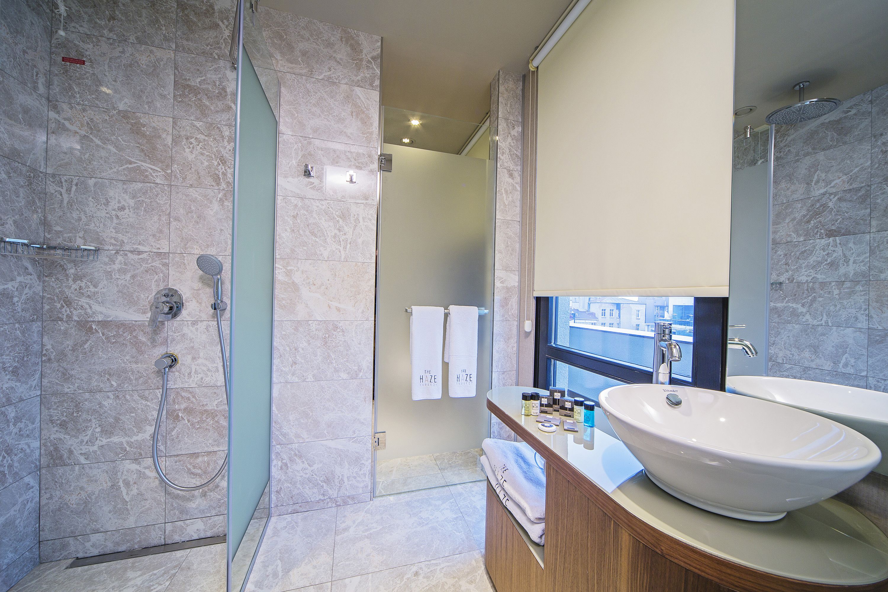 A modern bathroom with a large sink, a glass shower enclosure, and a view of the city through a window.