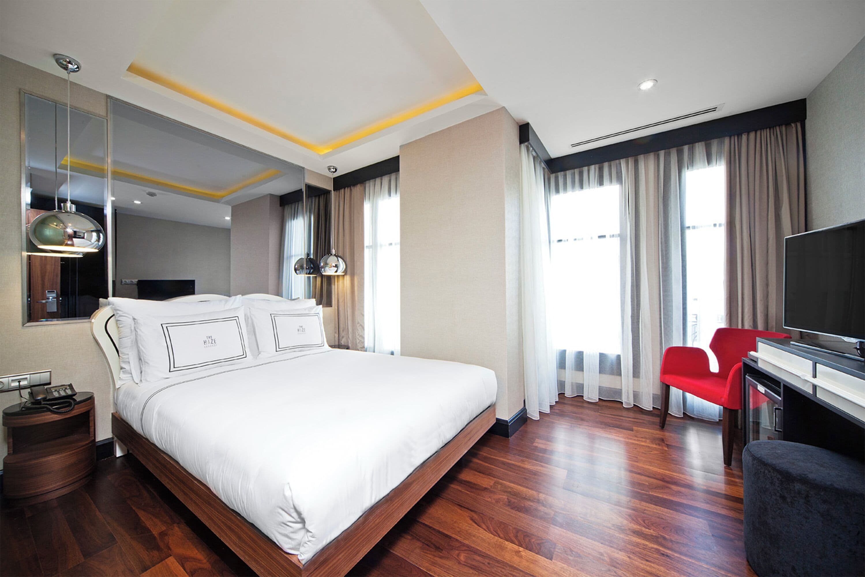 Habitación de hotel moderna con una cama grande, un escritorio con televisor de pantalla plana y una silla roja.