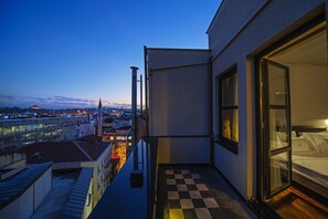 Habitación de hotel con piso a cuadros, una cama y vista a la ciudad al atardecer.
