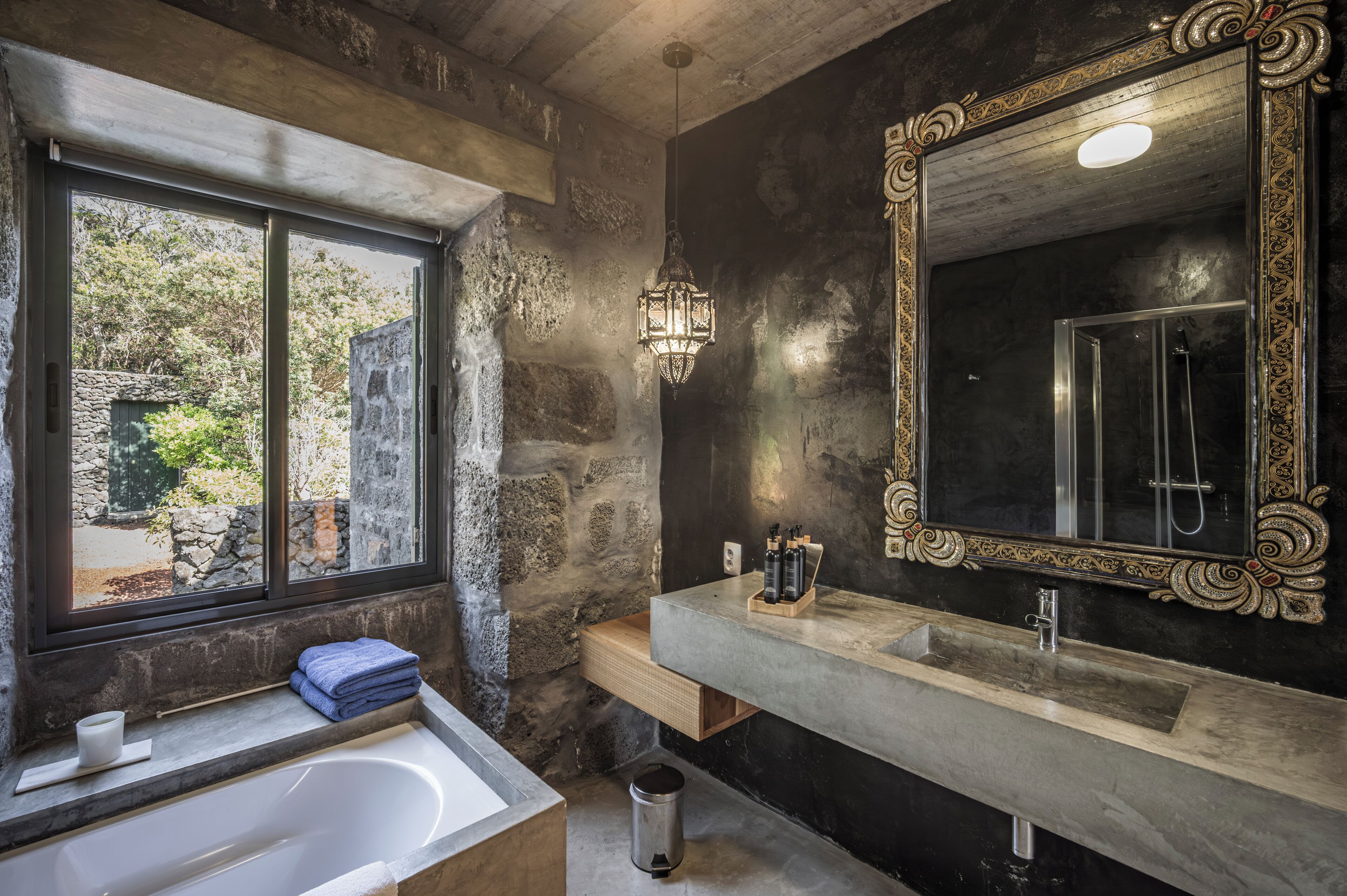 Un baño moderno con un ventanal grande, una bañera, un tocador con espejo y una pared de piedra.