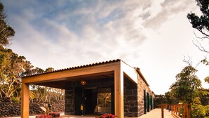 A modern house with a wooden deck, stone walls, and a garden with rocks and plants. - Pocinhobay (Madalena)