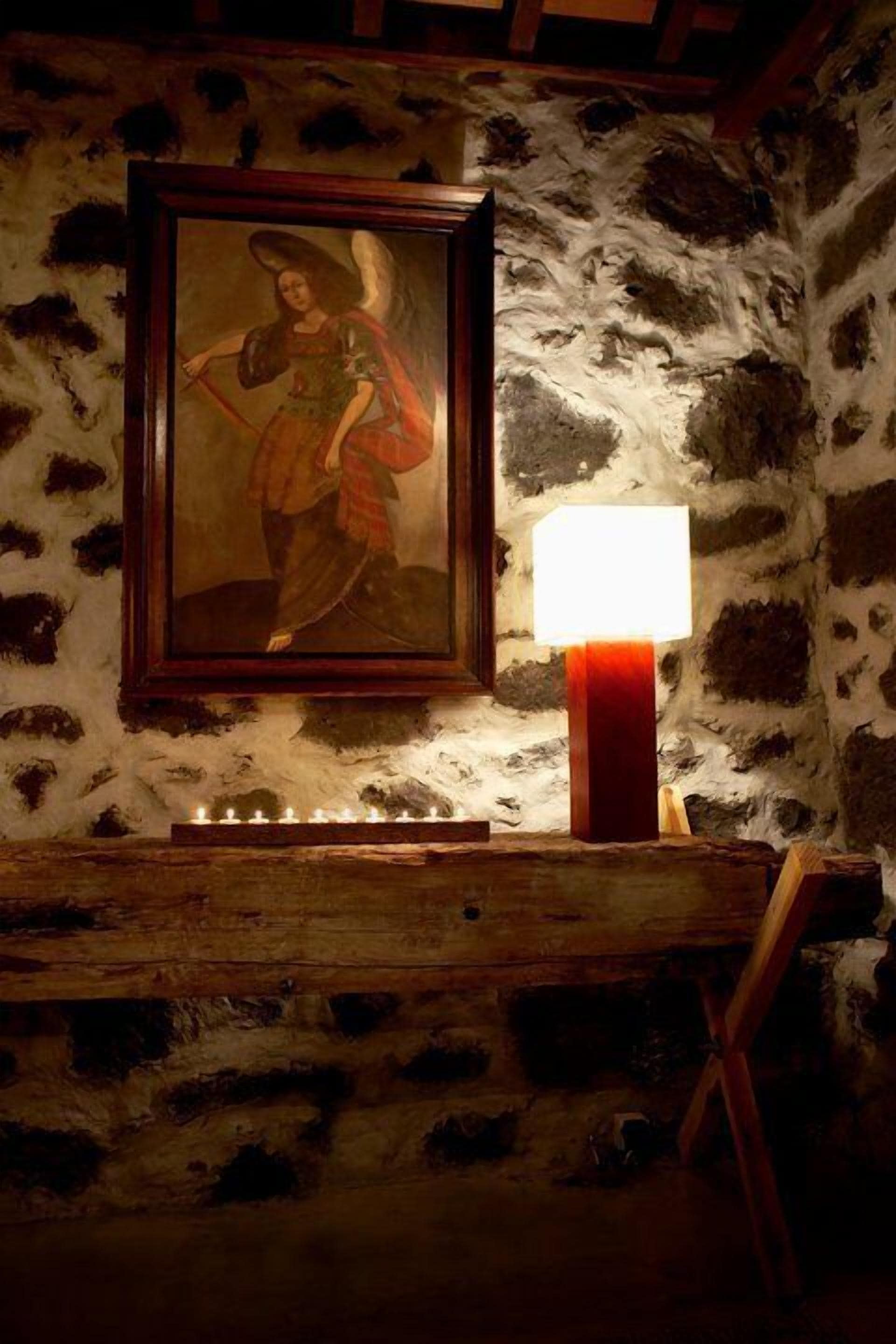 Una stanza rustica con parete in pietra, un quadro incorniciato, una panca di legno e una lampada da tavolo.