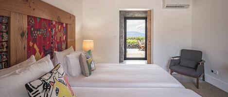 A hotel room with a wooden ceiling, a bed with white bedding, a chair, and a view of the outdoors.