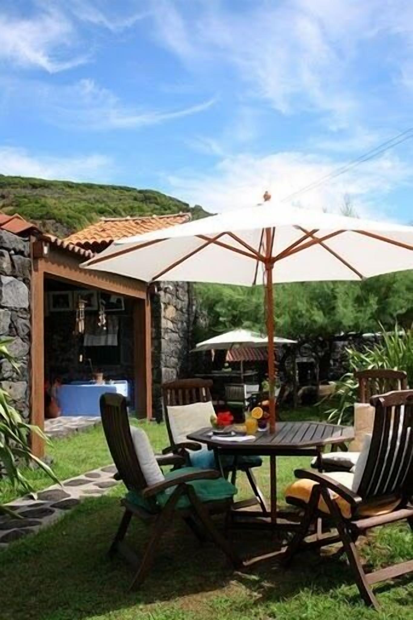 Un patio al aire libre con un muro de piedra, una mesa con sillas y un paraguas grande.