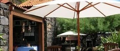 Un patio al aire libre con un muro de piedra, una mesa con sillas y un paraguas grande.
