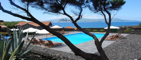 Una piscina al aire libre, sombrillas, sillones reclinables de piscina