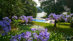 Una piscina rodeada de exuberante vegetación y flores moradas, con vista a un lago y colinas distantes.