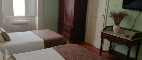 A room with two beds, a wooden wardrobe, a desk with a vase, and a television on the wall.