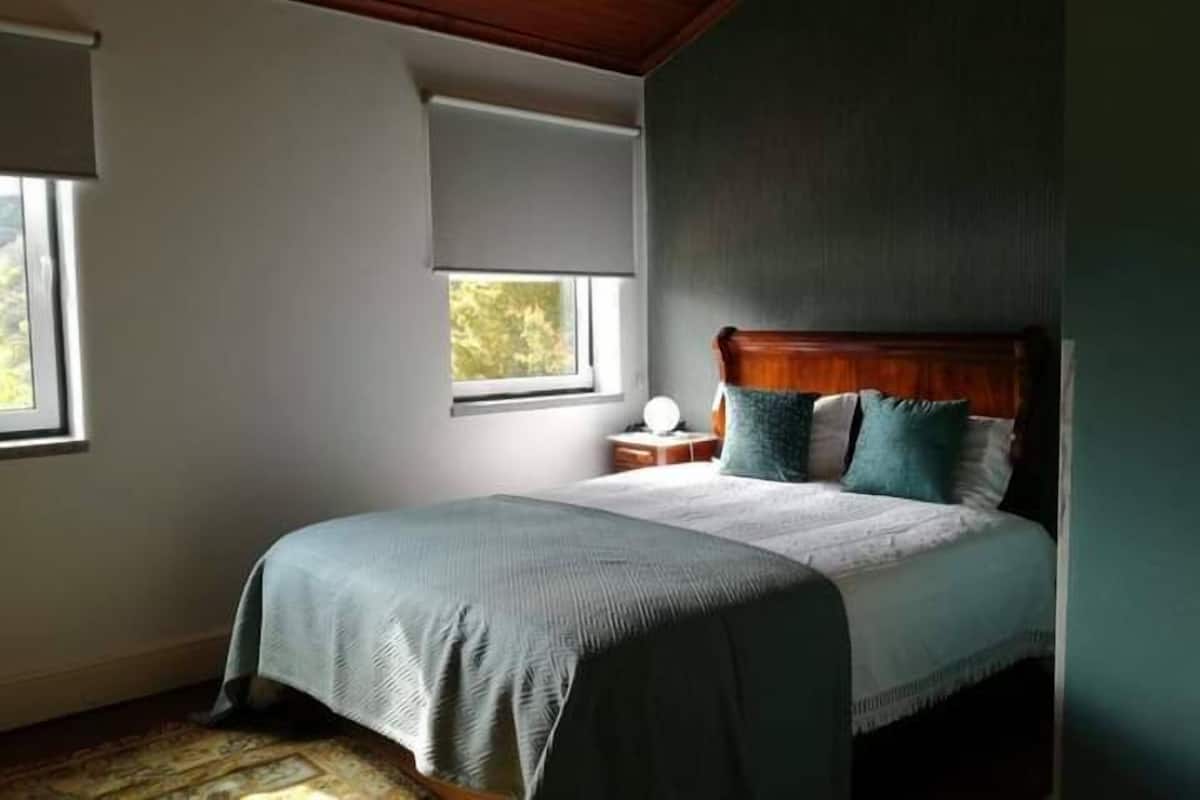 Une chambre à coucher comprenant un lit, une table de chevet, une fenêtre et un plafond avec des poutres en bois.