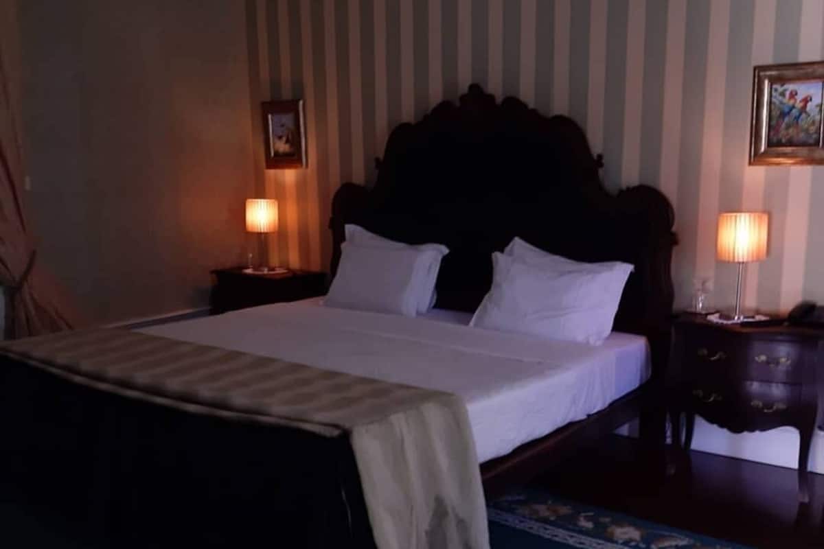 Un lit bien fait, avec du linge de lit blanc, une tête de lit en bois foncé et deux lampes de chevet.