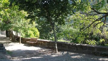 Un sentier dallé, agrémenté de bancs et bordé d’un muret en pierre, le tout entouré d’arbres et de verdure.
