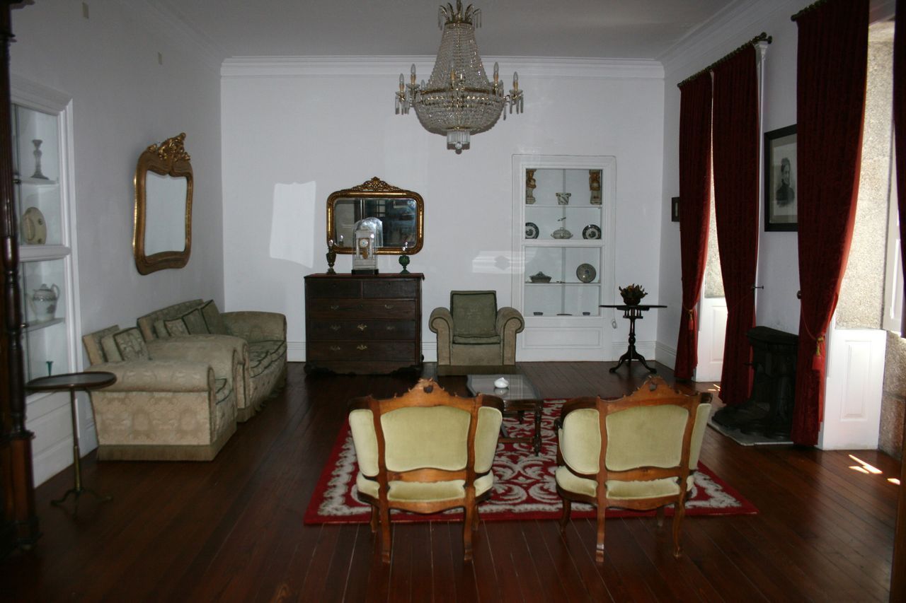 Een klassieke woonkamer met een kroonluchter, een zithoek, een eettafel met stoelen, een open haard en een spiegel aan de muur.