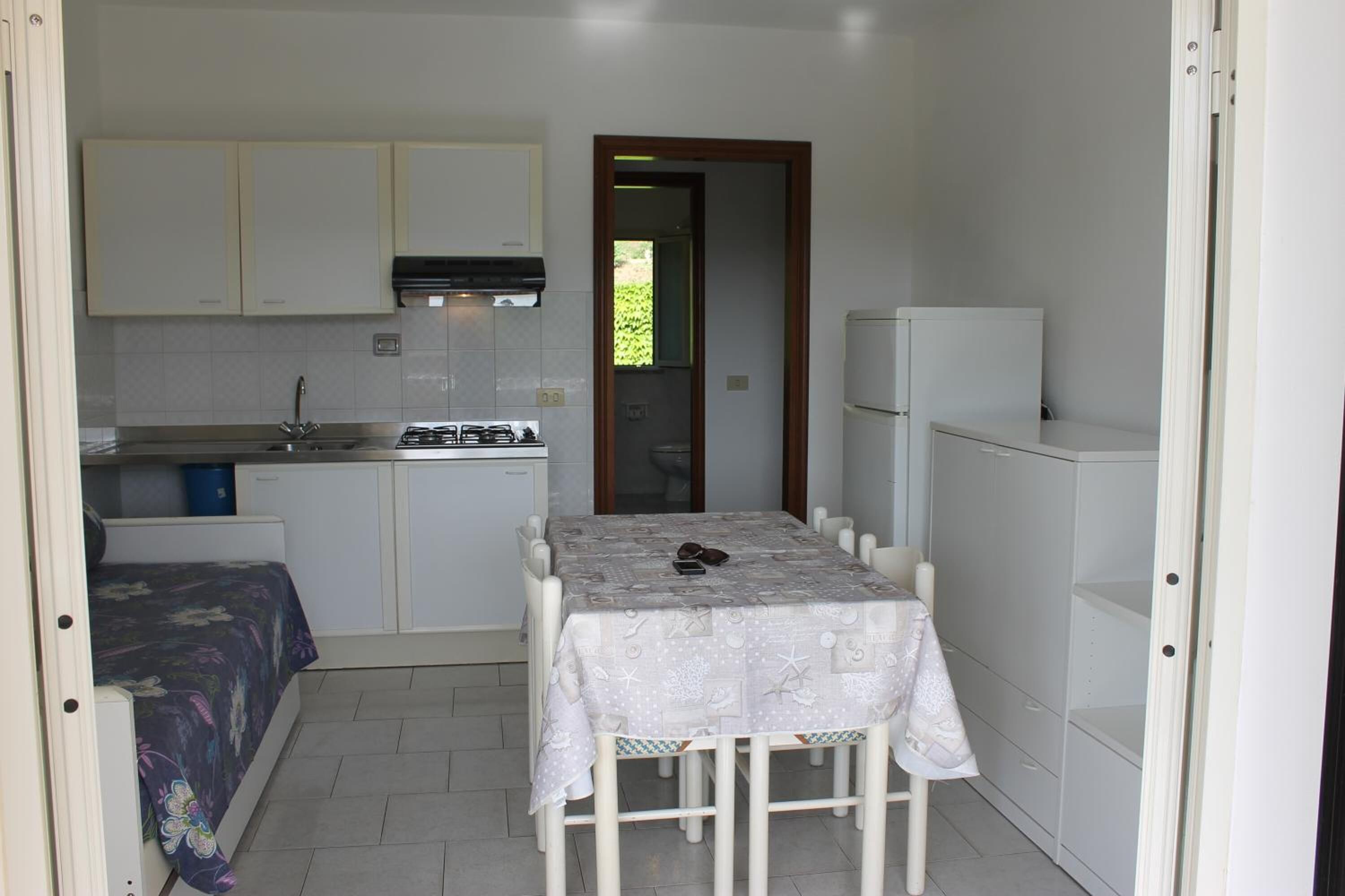 A compact kitchen with white cabinets, a gas stove, a sink, and a table with a tablecloth.