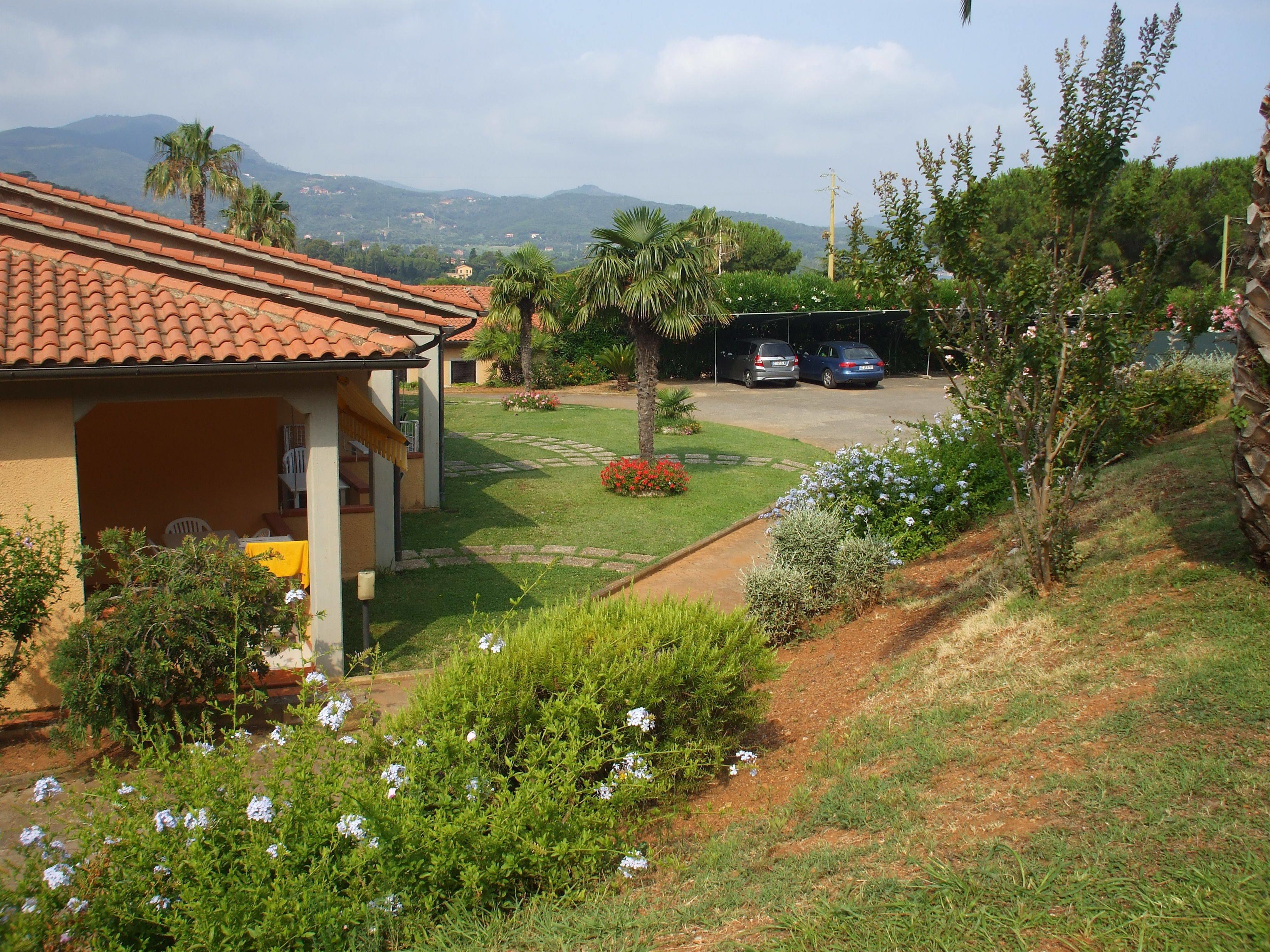A residential area with a house featuring a tiled roof, a small garden with flowers, and a paved driveway.