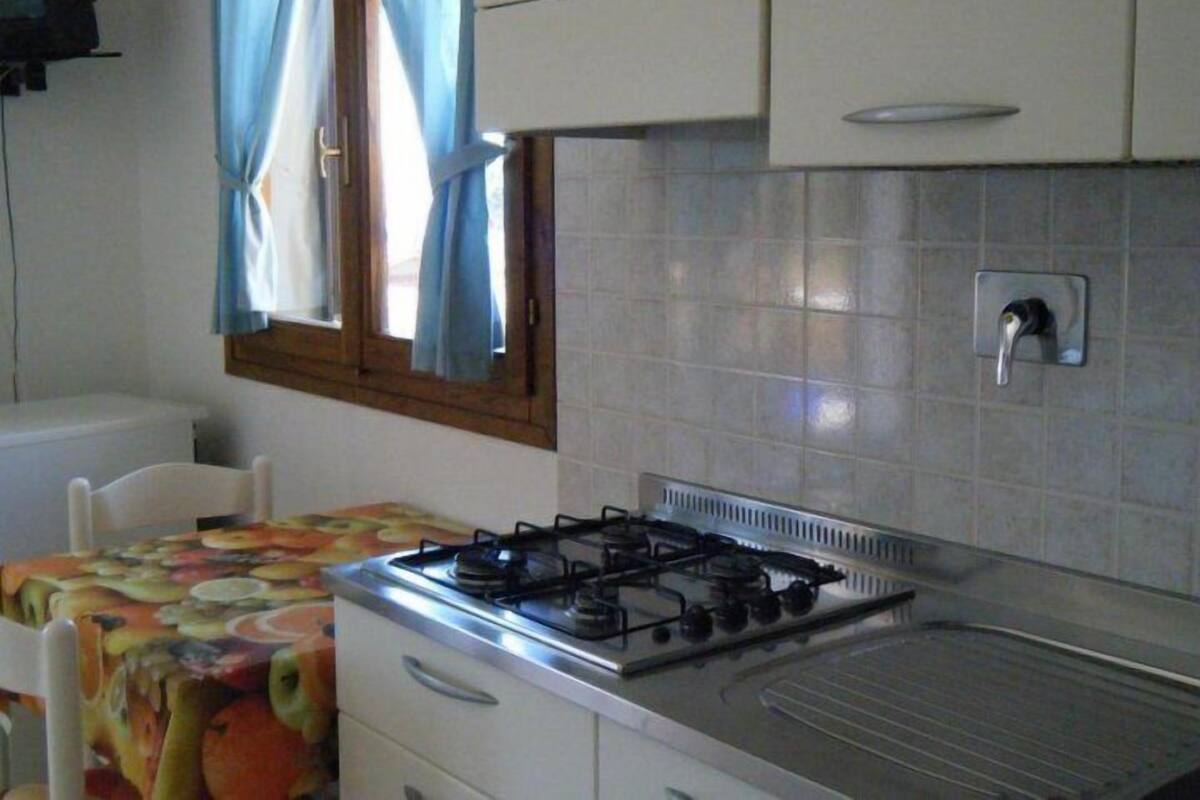 A compact kitchen with a gas stove, a small sink, and a window with curtains.