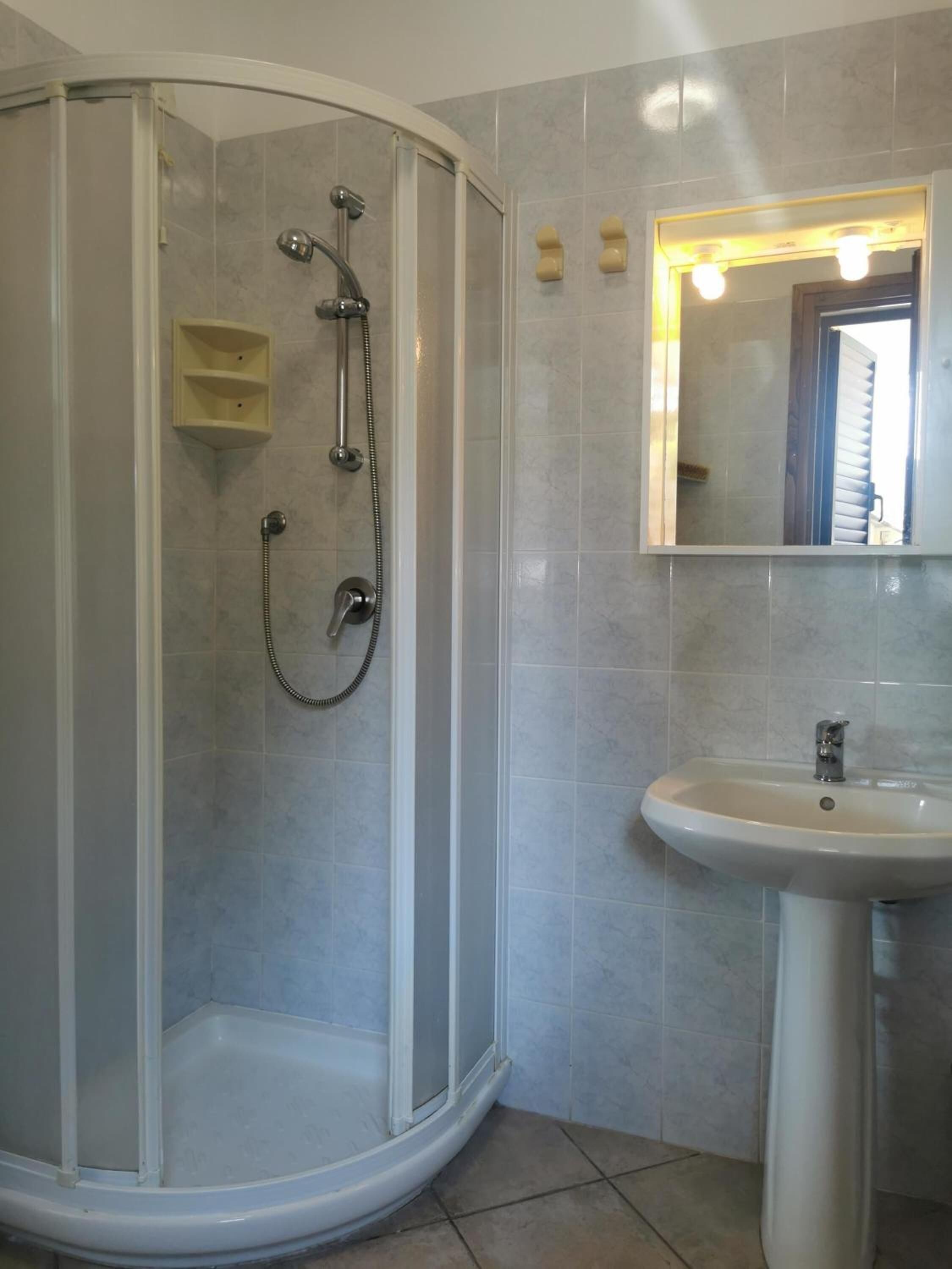 Een badkamer met een douchecabine van glas, een wastafel en een spiegel.