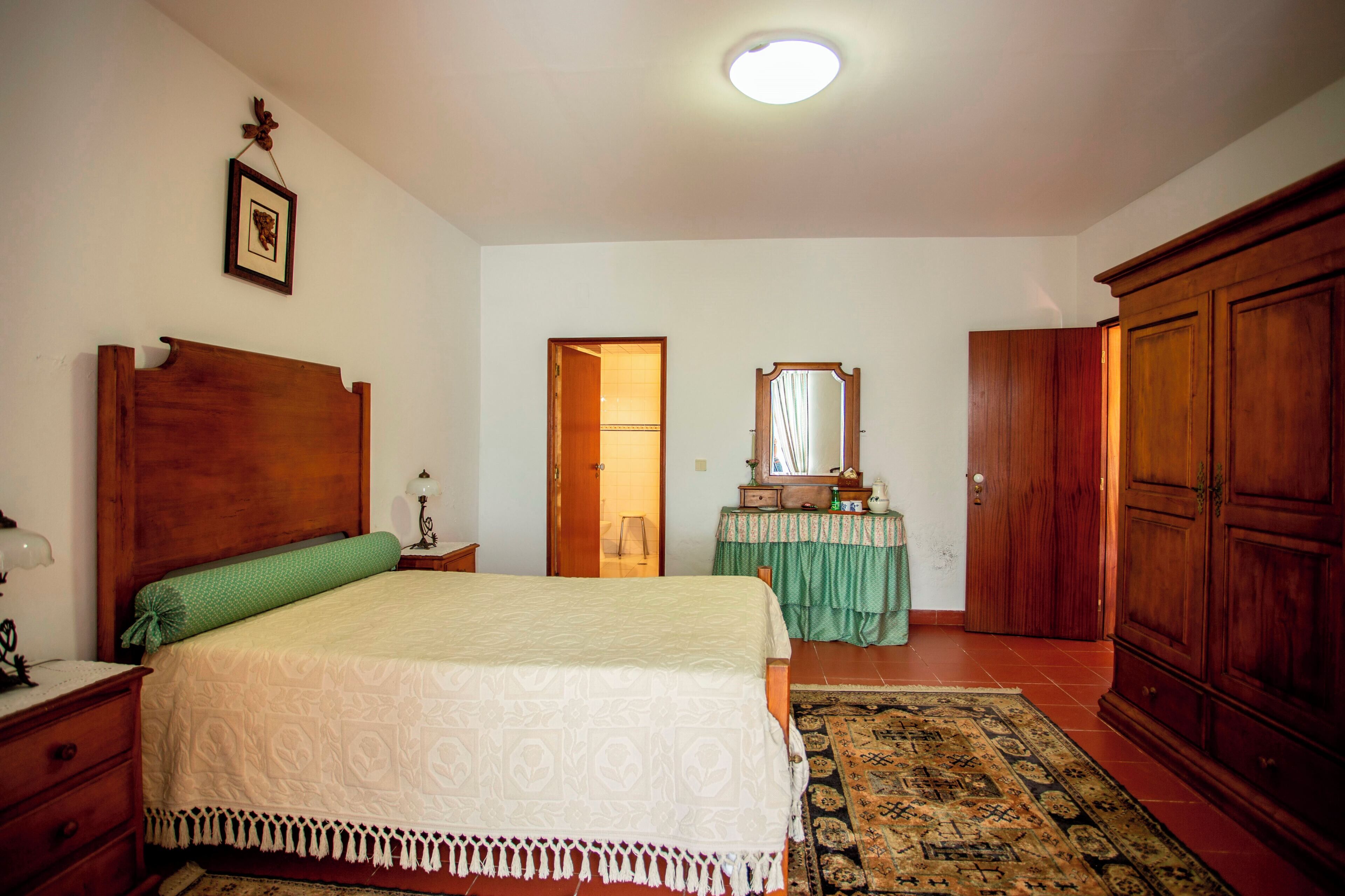 Un dormitorio con cama de madera, mesita de noche, espejo, armario y cómoda cubierta con mantel verde.
