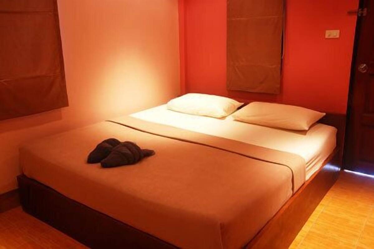 Uma cama de solteiro com travesseiro branco e cobertor escuro, piso de madeira e porta com puxador.